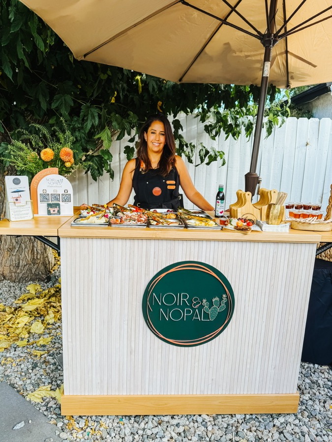 Tatiana serving a full charcuterie spread from a Noir & Nopal branded cart