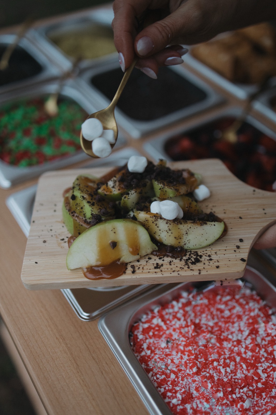 Apple slices with caramel, cookie crumble, and mini marshmallows, with a red and white topping visible nearby
