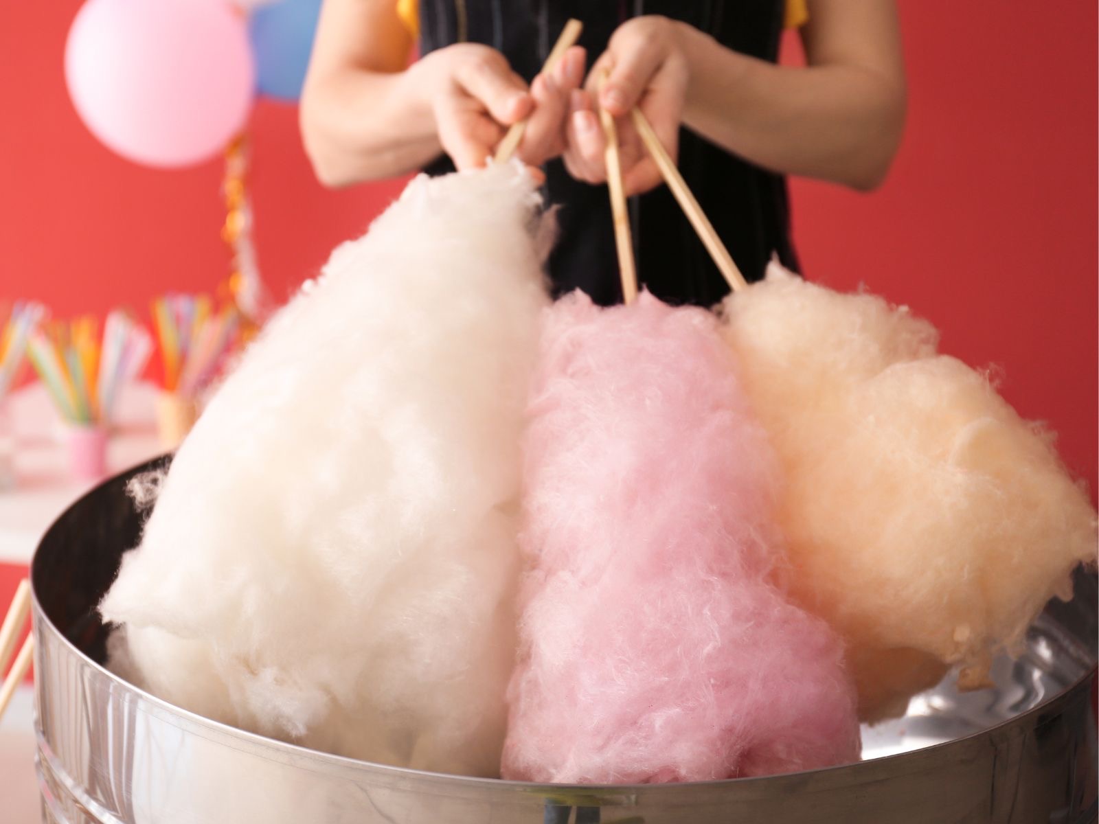Cotton candy in white, pink, and orange spun onto sticks, held above a cotton candy machine