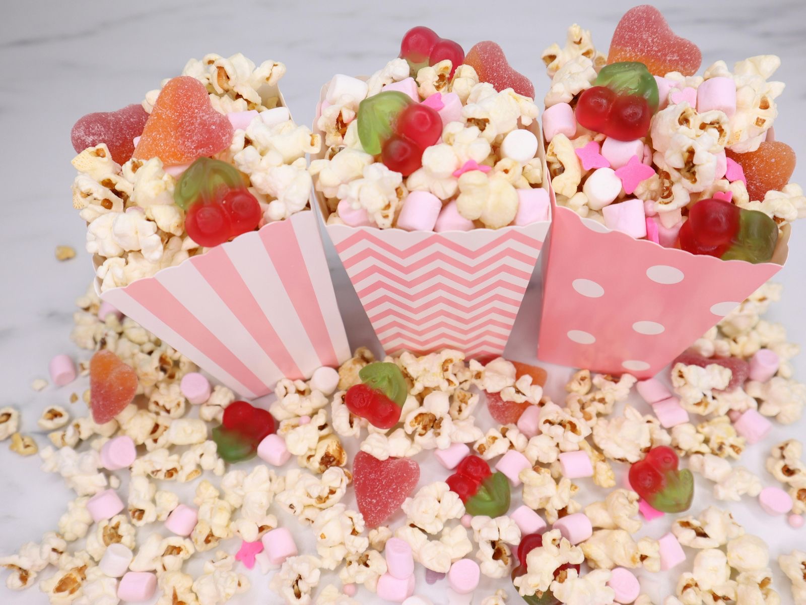 Popcorn mixed with mini marshmallows and fruit-shaped gummy candies in striped paper cups