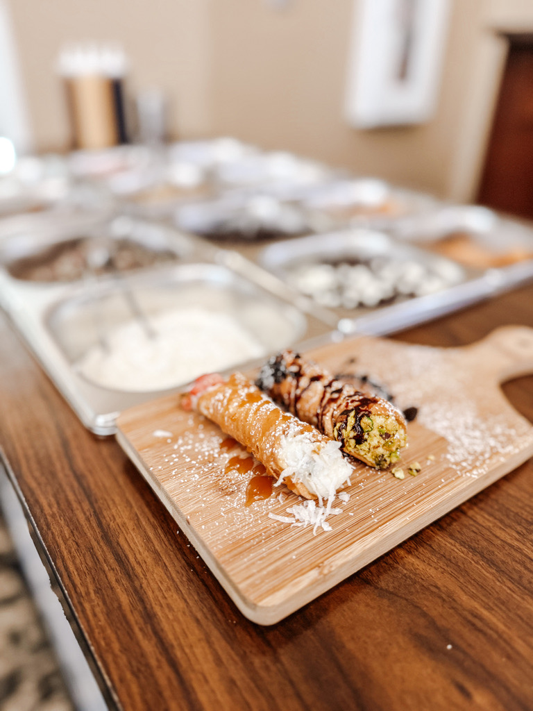 Two finished cannoli on a serving board, with the topping bar visible behind