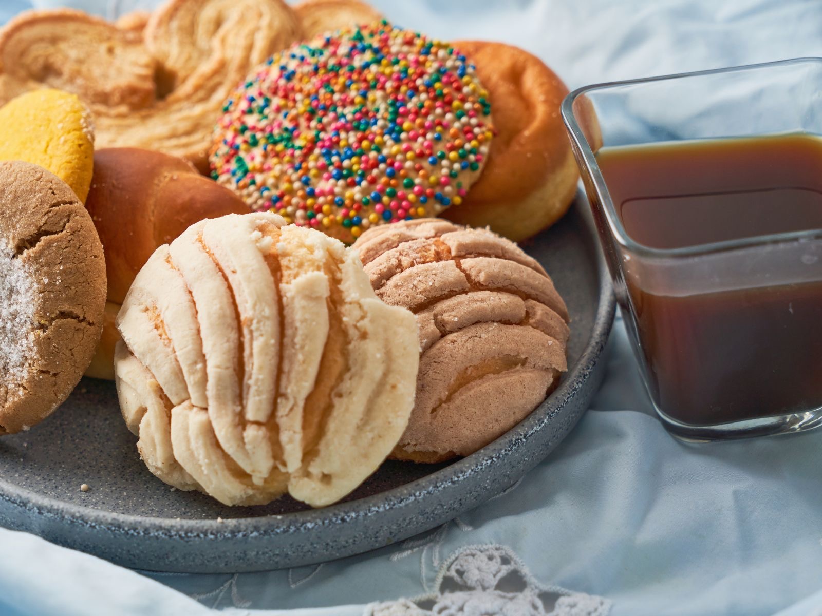A plate of Mexican pan dulce, conchas and other pastries, with a glass of cafe de olla