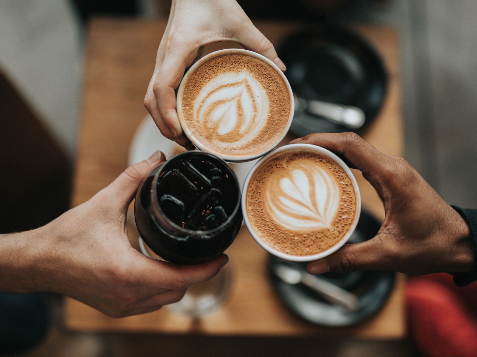 Three hands holding coffee drinks together in a toast, latte art visible