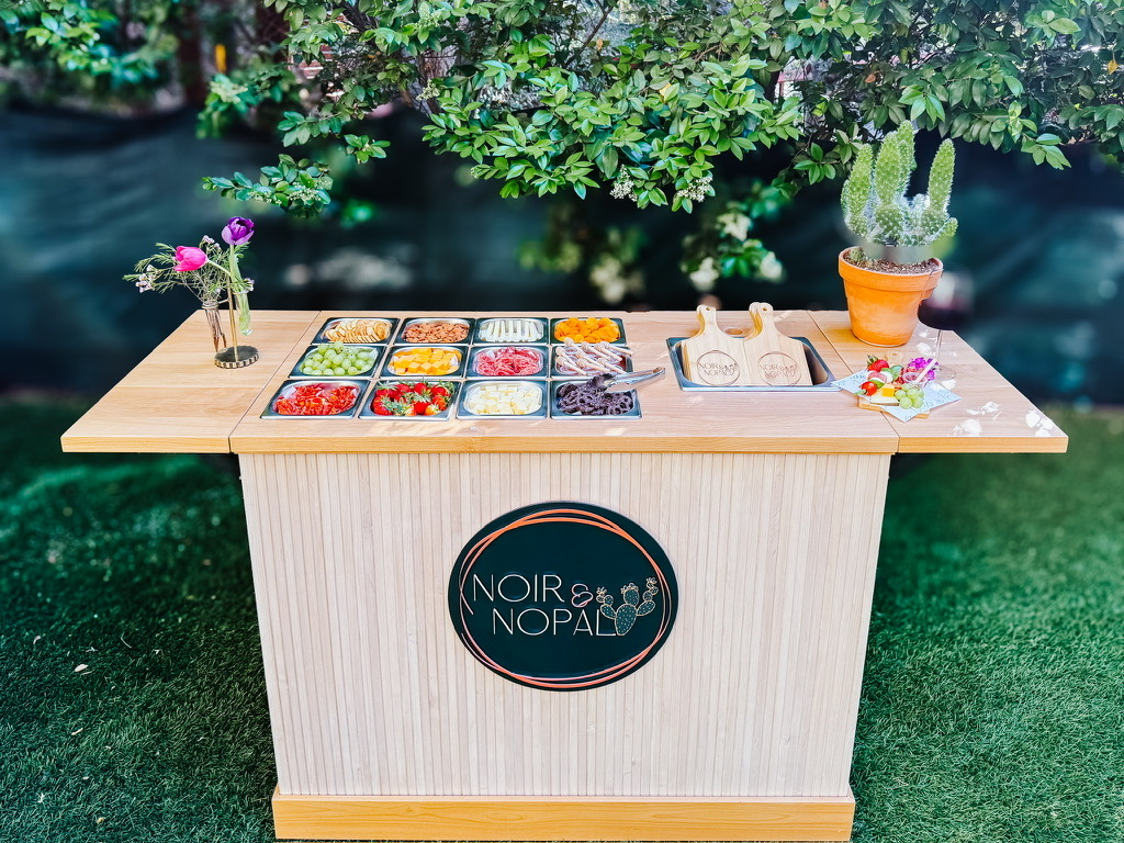 The Essentials charcuterie cart styled and stocked before guests arrive, set outdoors under greenery