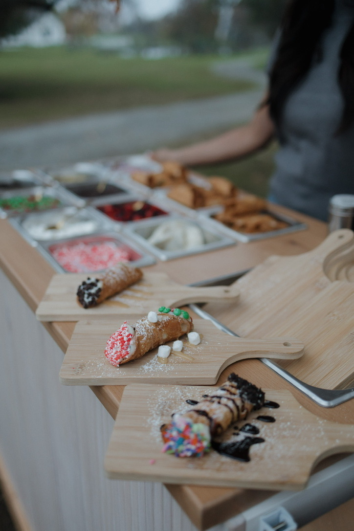 Three finished cannoli on serving boards, with the topping bar and staff visible behind