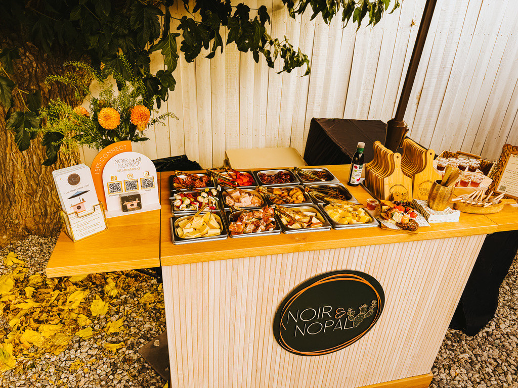 The Noir Edit luxury charcuterie cart styled and fully stocked, set outdoors with florals and signage