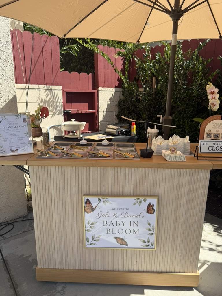 The styled Luxe Mini Pancake Stack cart and topping bar set up under an umbrella for a real event